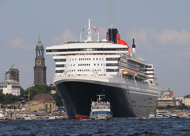 Hamburgfotos - Bilder von der Queen Mary 2 auf der Elbe - Hamburger Michaeliskirche  011_59_4382 Die Queen Mary 2 auf der Elbe vor den St. Pauli Landungsbrcken; lks. die Kuppel vom Eingangsgebude des Alten Elbtunnels, dahinter der hohe Kirchturm des Hamburger Michels und rechts die schwedische Gustav-Adolf-Kirche. Viele Barkassen, Schiffe der Hafenrundfahrt und private Sportboote / Motorboote begleiten den gewaltigen Luxusliner bei  seiner Fahrt auf der Elbe; auch an den Landungsbrcken stehen die Schaulustigen dicht gedrngt.  www.hamburg-fotograf.com