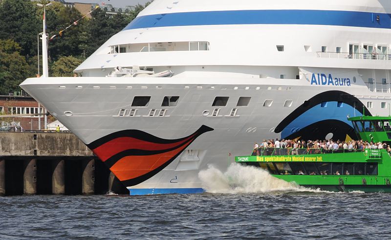 Schiffsbilder aus der Hansestadt Hamburg - Kussmundbug des Kreuzfahrtschiffs Aida Aura, Altona.  011_63_4801 Das Passagierschiff Aida Aura hat als erstes Kreuzfahrtschiff das Terminal Hamburg-Altona angelaufen. Die Aida Aura wurde 2003 fertig gestellt und hat eine Lnge von 2002 m sowie eine Breite von 28 m. Das Schiff kann 633 Passagiere an Bord nehmen und hat eine Besatzung von 418 Mann. Ein Schiff der Hafenrundfahrt fhrt nahe an den mit einem Kussmund bunt bemalten Bug heran - Hamburgtouristen stehen auf dem Deck und betrachten das Kreuzfahrtschiff;  www.hamburg-fotograf.com