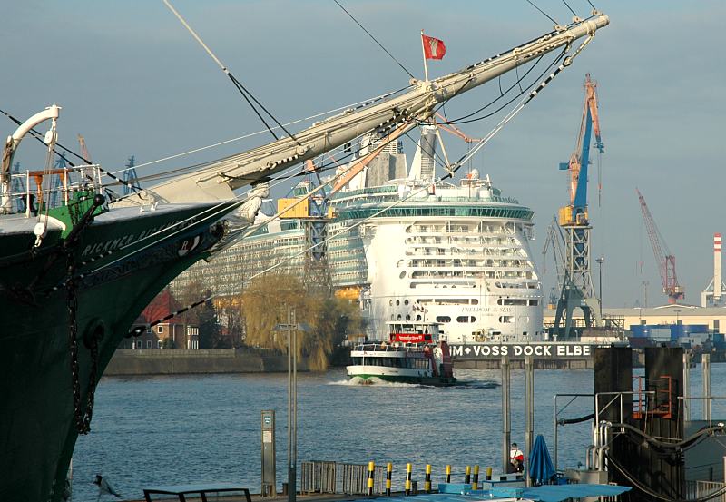 Hamburger Fotograf - Hamburg-Bilder aus dem Hafen - Bug der RICKMER RICKMERS, Passagierschiff FREEDOM OF THE SEAS.  011_71_6746 DHinter dem Vordersteven des Museumschiffs RICKMER RICKMERS liegt das Passagiertschiff FREEDOM OF THE SEAS im Trockendock der Hamburger Werft Blohm + Voss. Eine Hafenfhre kreuzt die Elbe vor den St. Pauli Landungsbrcken, um dort anzulegen. 