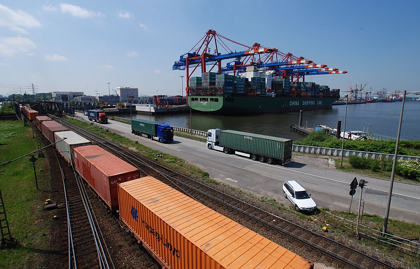 011_15761 Blick ber den Waltershofer Damm zum Eurogate Terminal - ein beladener Container Carrier liegt am Kai - alle Containerbrcken sind herunter gefahren und entladen das Schiff. Im Vordergrund ein langer Containerzug und auf der Strasse Lastwagen mit ihrer Containerladung. www.fotograf-hamburg.de