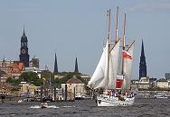 011_26079 Hamburg Panorama mit Kirchtrmen der Hansestadt Hamburg - links der Michel, dann der Turm der St. Petrikirche, danach die St. Jakobikirche, rechts die hohe Turmruine der St. Nikolaikirche die als Mahnmal stehen gelassen wurde - davor der kleine Turm der Gustav-Adolf-Kirche. Im Vordergrund der 1907 in Norwegen gebaut Heringslogger LOTH LORIEN unter Segeln. www.hamburg-fotograf.com