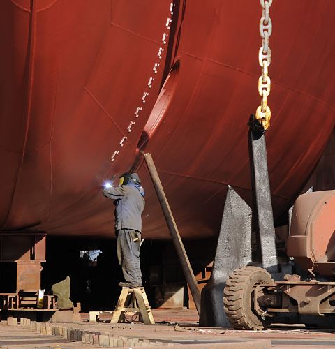 Fotos von der Arbeit im Hamburger Hafen / Schweisser Werft 011_26099 Ein Schweisser arbeitet im Trockendock der Werft an einem Schiffsrumpf. ber ihm sind die Markierungen fr den Tiefgang des Schiffes zu erkennen. Auf dem Boden steht der Anker des Schiffes. www.hamburg-fotograf.com