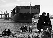 11_17453 Fotos vom Hamburger Hafen - das Containerschiff CMA CGM Carmen wird  hoch beladen von zwei Schleppern in den Hamburger Hafen gebracht - der Containerriese hat eine Lnge von ca. 300m und eine Breite von 40m; der Frachterf kann 6627 TEU / 20 Fuss Container als Ladung an Bord nehmen. Am Elbstrand stehen und sitezen Hamburger, die das Schiffsmanver interessiert beobachten.   www.christoph-bellin.de