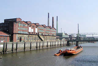 P1010083 Eine Schute wird von einem Schlepper im Müggenburger Kanal gezogen - am Ufer historische Industrie-Ziegelgebäude auf der Peute in Hamburg Veddel.
