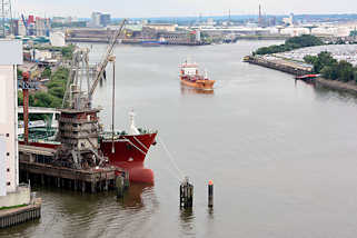 8689 Blick auf die Rethe in Hamburg Wilhelmsburg - ein Frachtschiff fhrt Richtung Khlbrand / Sderelbe; im Vordergrund wird die Ladung eines Massengutfrachters gelscht.