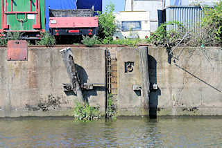 5886 Kaimauer am Tidekanal in Hamburg Billbrook; Streichdalben aus Holz, verrottet - Eisenleiter in der Kaimauer; abgestellte LKW, Wohnwagen.