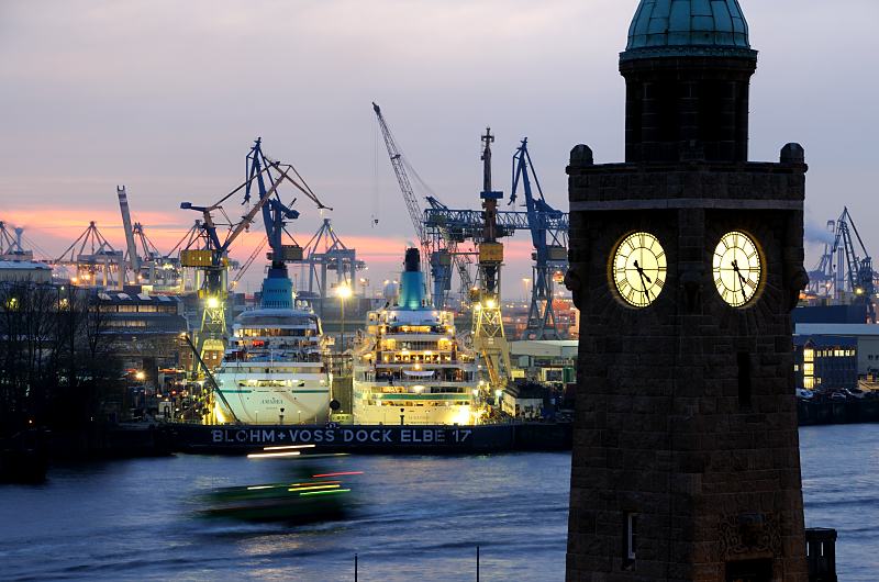 Fotograf Hamburg; Uhr- und Pegelturm der St. Pauli Landungsbrcken bei Nacht - Schiffe im Trockendock.  011_67_4525 DBlick von den St. Pauli Landunsbrcken ber die Elbe zum Blohm + Voss Dock Elbe 17. Die beiden Passagierschiffe AMADEA und ALBATROSS haben fr Wartungsarbeiten in der Hamburger Werft eingedockt. Die Schiffe sind hell angestrahlt - es wird auch nachts an ihnen gearbeitet. Im Vordergrund der Uhrturm / Pegelturm; die Zifferbltter sind erleuchtet. 