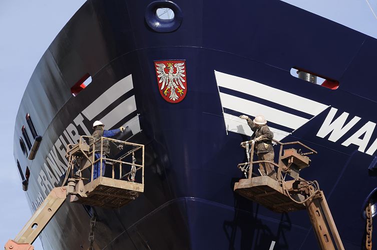 Hafenfotografie von der Arbeit im Hamburger Hafen / Schiffsbug der Wappen von Frankfurt  011_26100 Zwei Hafenarbeiter stehen im Trockendock auf Hebebhnen und malen mit weisser Farbe  den Schriftzug "Wappen von Frankfurt" auf den Bug des Schiffs. In der Mitte ist das Wappen der Stadt aufgebracht; es zeigt in Rot einen gekrnten silbernen Adler. www.hamburg-fotograf.com