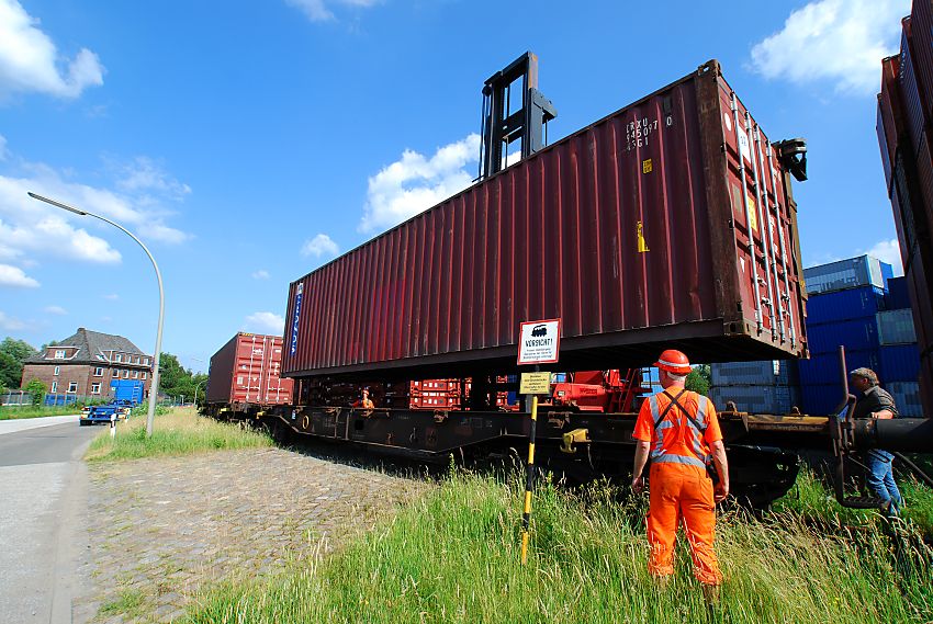 011_15723 Beladung eines Gterzugs mit Containern im Hafengebiet Hamburgs - ein Portalhubwagen holt den Container vom Lager und senkt ihn vorsichtig auf den Gterwaggon. Nachdem der Container seine Platz gefunden hat, fhrt die Lokomotive den Gterzug einen Waggon vor, damit der nchste leere Wagen beladen werden kann. Hafenarbeiter berwachen den Vorgang.  www.fotograf-hamburg.de