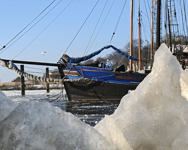 Winter im Museumshafen Oevelgoenne - Eisschollen + Segelboot.  011_26074 Eisschollen am Ufer der Elbe vom Museumshafen Hamburg Oevelgoenne - die Wintersonne scheint auf das Eis. Eins historisches Segelboot liegt an seinem Liegeplatz im Hafen und berwintert dort. Das Wasser der Elbe ist gefroren. www.hamburg-fotograf.com