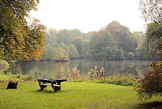 5734 Herbstlich gefrbte Bume am Mhlenteich in Grosshansdorf; Herbstfarben. Sitzbank / Sitzgruppe aus Holz, Picknickplatz auf einer Wiese am Wasser.