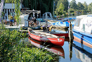 5420 Bootsvermietung  am Stadtsee von Mlln - ein rotes Kanu liegt am Schilf des Sees - im Hintergrund Tretboote.