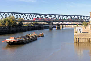 2660 S-Bahnzug in Fahrt auf der Eisenbahnbrcke ber den Oberhafenkanal / Billehafen in Hamburg Rothenbursort; eine Schute wird auf dem Kanal von einer Barkasse gezogen.