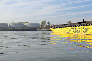 7530 Hafenbecken Petroleumhafen im Hamburger Hafen - ein gelber Leichter mit der Aufschrift Containertaxi liegt an der Spundwand, am Ufer ltanks.