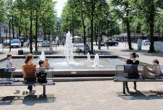 8864 Sprudelnder Brunnen - Zentrum von Ahrensburg, Kreis Stormarn. Familien sitzen in der Sonne auf Bnken am Brunnenbecken.