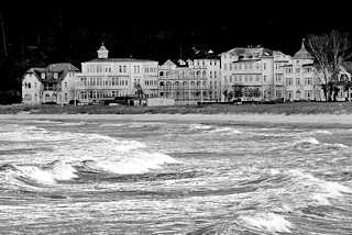 5633 Wellen und Gischt - windiger / stürmischer Tag an der Ostsee - im Hintergrund die Strandpromenade mit Gebäuden.