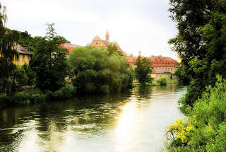 2808 Ufer der Regnitz in Bamberg - Bäume und Sträucher am Wasser; im Hintergrund das Stadtarchiv und das Hotel Residenzschloss Bamberg.