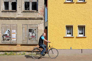 9441 Restauriertes Wohnhaus mit gelb gestrichener Fassade, verfallenes Gebäude mit abbröckelndem Putz und Luken verschlossene Fenster - Fahrradfahrer; Architekturbilder aus Barth  / Alt + Neu.
