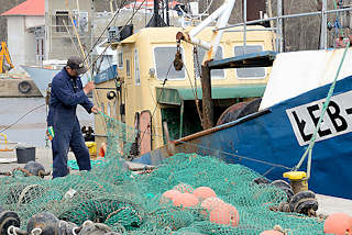 0894 Fischereihafen an der Ostsee in Łeba, Polen - ein Fischer repariert ein Netz; Fischkutter am Kai. 