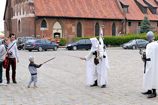 5108 Hof der Ordensburg in Malbork / Marienburg, Polen. Als Ordensritter verkleidete Männer spielen mit einem Kind Schwertkampf.