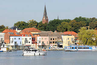 9226 Wohnhäuser an der Hafenpromenade von Malchow am Malchower See - ein Ausflugsschiff legt ab; Kirchturm der Stadtkirche.