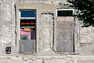 21_7632 Mit Spanplatten teilweise vernagelte Fenster, Neu Neu Neu! Musterausstellung zwischen abgebröckeltem Putz und mit Lehm verputzten Strohmatten gefüllten Fachwerk.