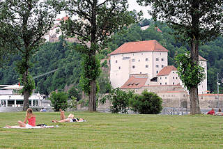 3130 Wiese auf der Landspitze an der die Inn in die Donau mündet - Menschen liegen auf Decken in der Sonne - am gegenüberliegenden Donauufer die Veste Niederhaus an der die Ilz in die Donau fliesst. 