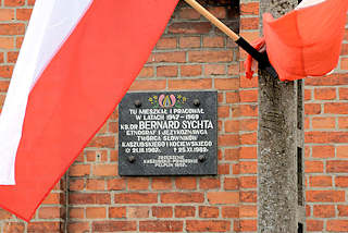 0013 Gedenktafel BERNARD SYCHTA in Pelplin, Polen - polnische Flaggen, weiss-rot. Bernard Sychta war Pfarrer an der Kathedrale von Pelplin und schrieb ein Kompendium über die Kultur der Kaschuben.