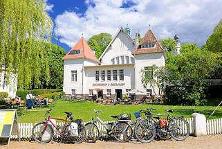 1848 Kulturforum Alte Schwimmhalle Plön; Aussengastronomie - Tische in der Sonne auf der Wiese; Fahrräder am Zaun - blauer Himmel, weisse Wolken