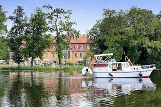 0730 Blick über die Havel bei Zehdenick - ein Motorboot fährt Richtung Schleuse; im Hintergrund das Havelschloss / Restaurant, Hotel.